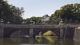 Eine Stebrücke über einem Fluss, im Hintergrund ein traditionelles Gebäude.