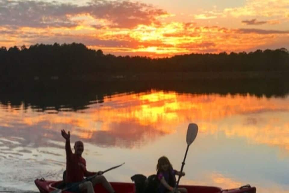 Un atardecer sobre un lago tranquilo con dos personas en una canoa roja.