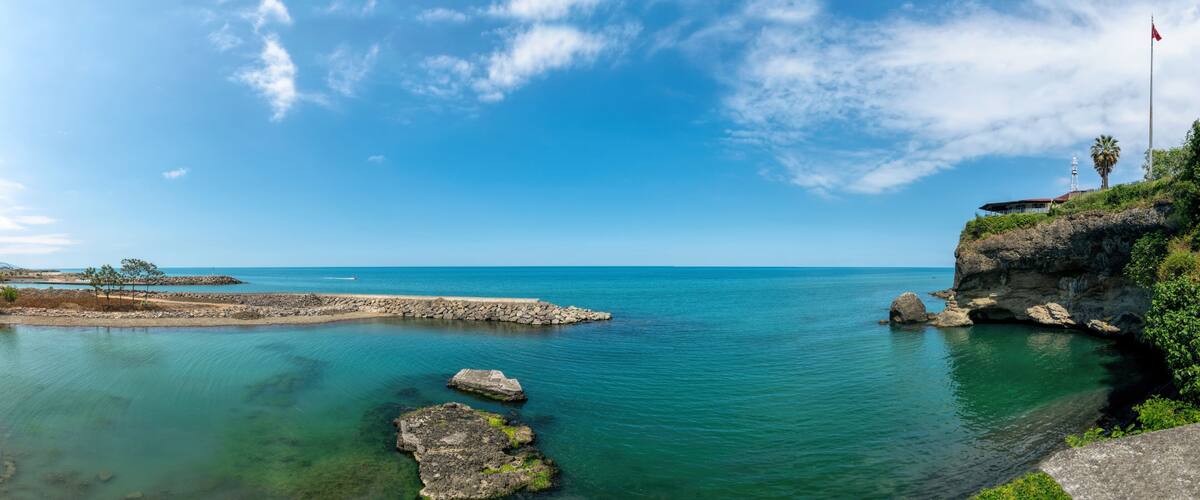 A coastal landscape with clear blue waters, rocky formations, and a flag on a cliff.