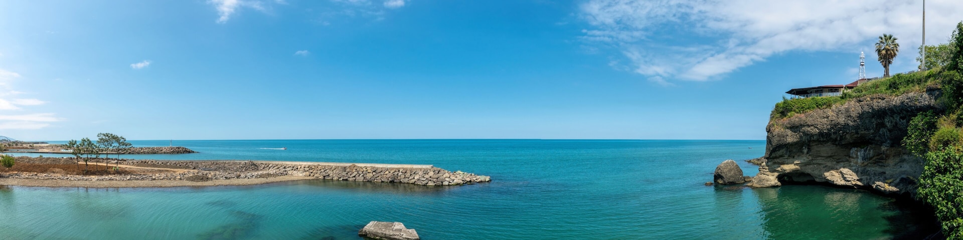 A coastal landscape with clear blue waters, rocky formations, and a flag on a cliff.
