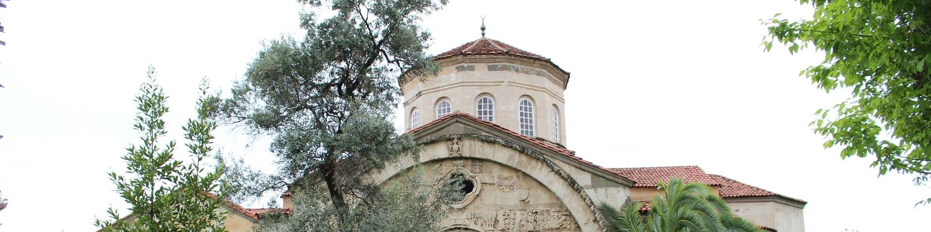 A historic building with a dome and arches, surrounded by well-maintained gardens and trees.