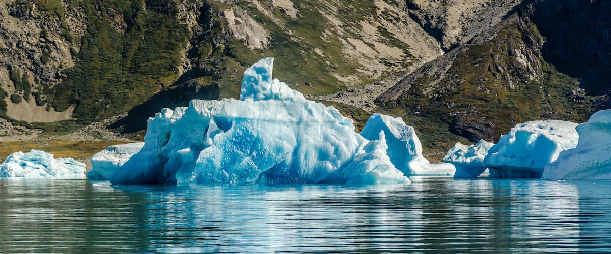 A glacier with large icebergs in a lake surrounded by mountains.