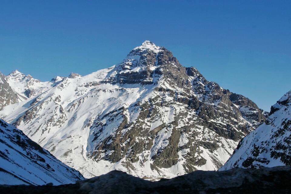 Ett snötäckt bergstopp med ett kargt landskap och en klarblå himmel.