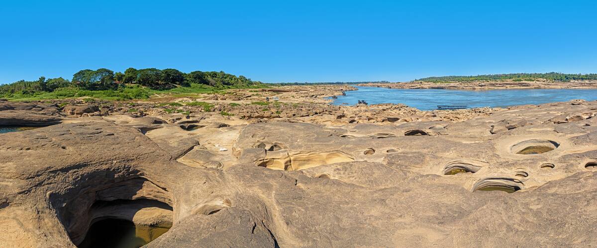 A rocky landscape with a river, a large cave, and distant trees.