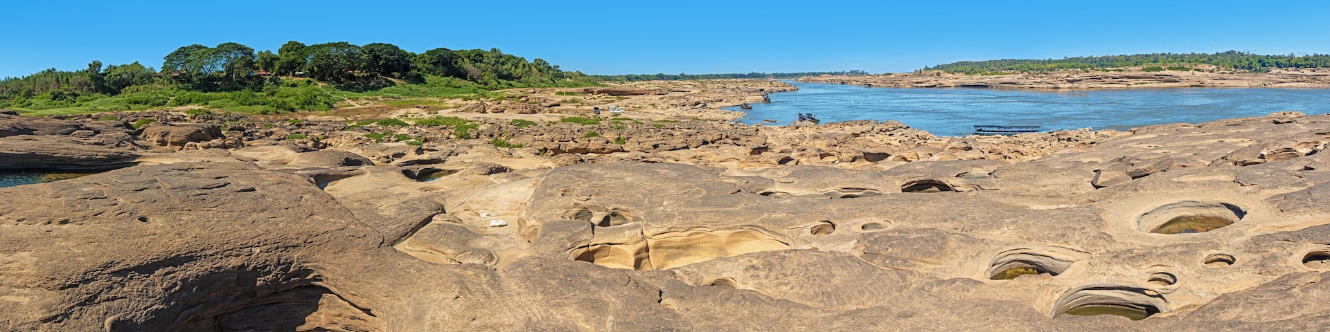 A rocky landscape with a river, a large cave, and distant trees.