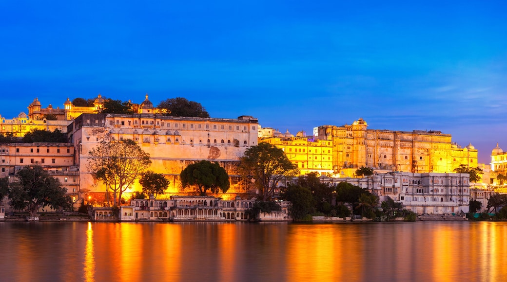 A grand illuminated palace complex by a calm lake at dusk.