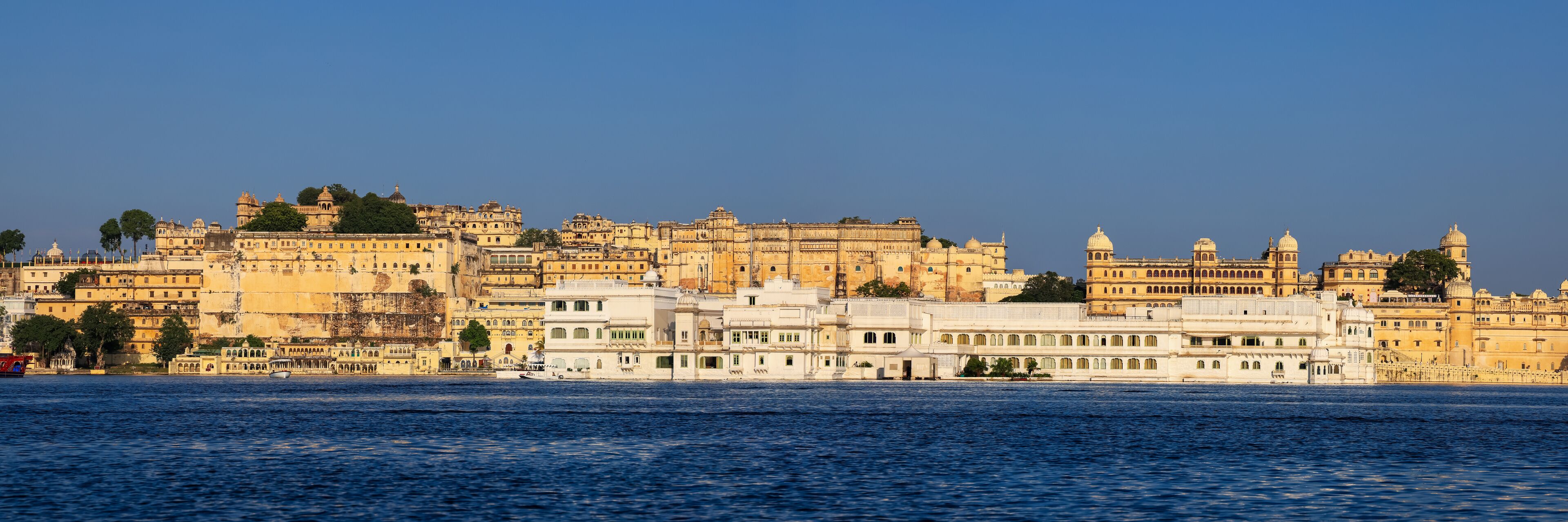 A historic cityscape with a river in the foreground and a large palace complex in the background.