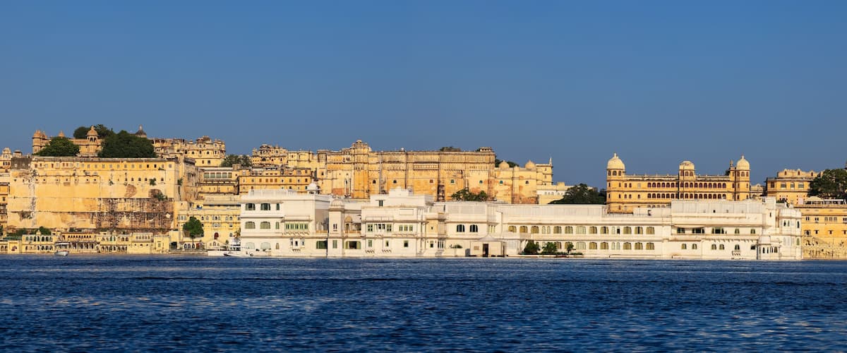 A historic cityscape with a river in the foreground and a large palace complex in the background.