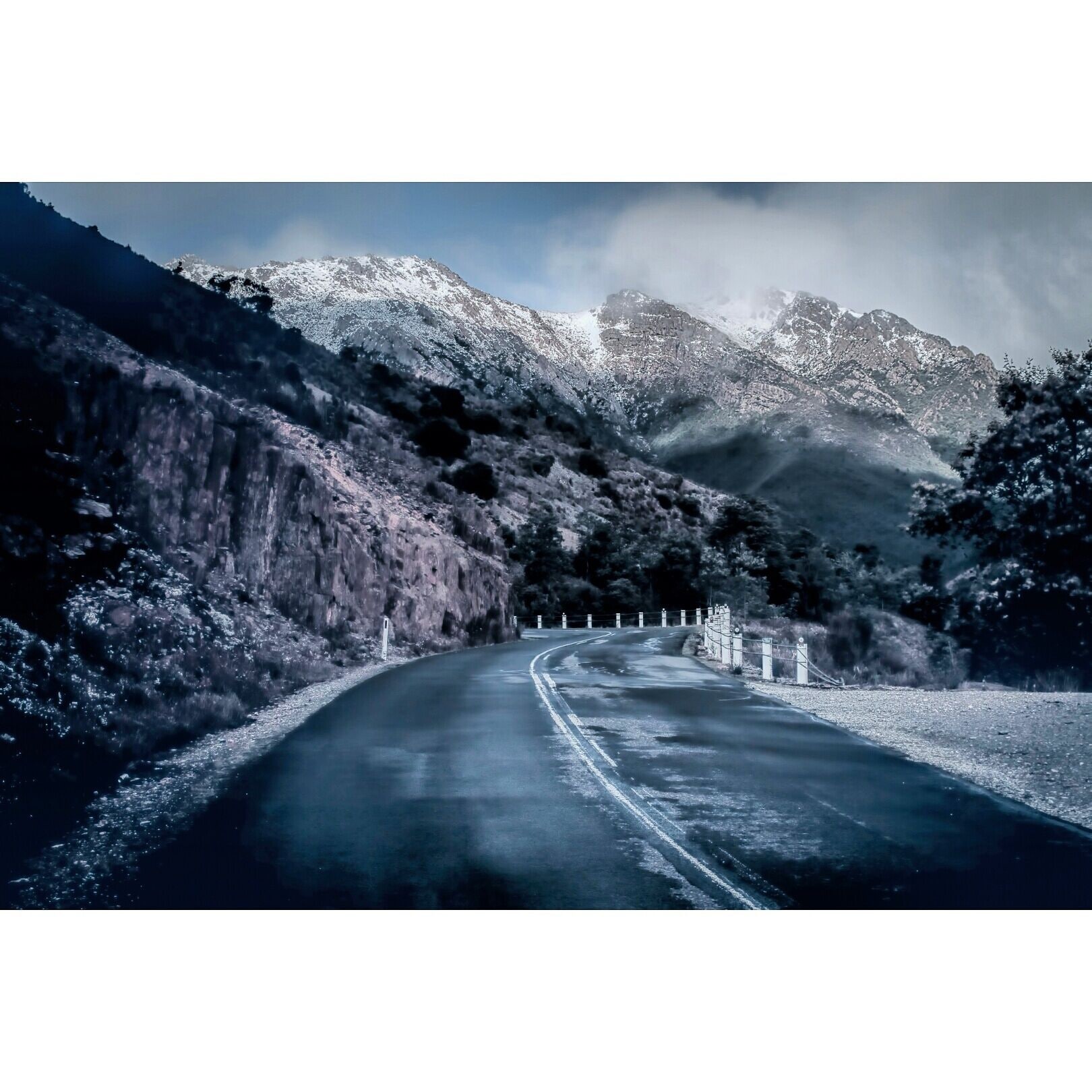 Una carretera sinuosa de montaña con laderas nevadas y acantilados rocosos.