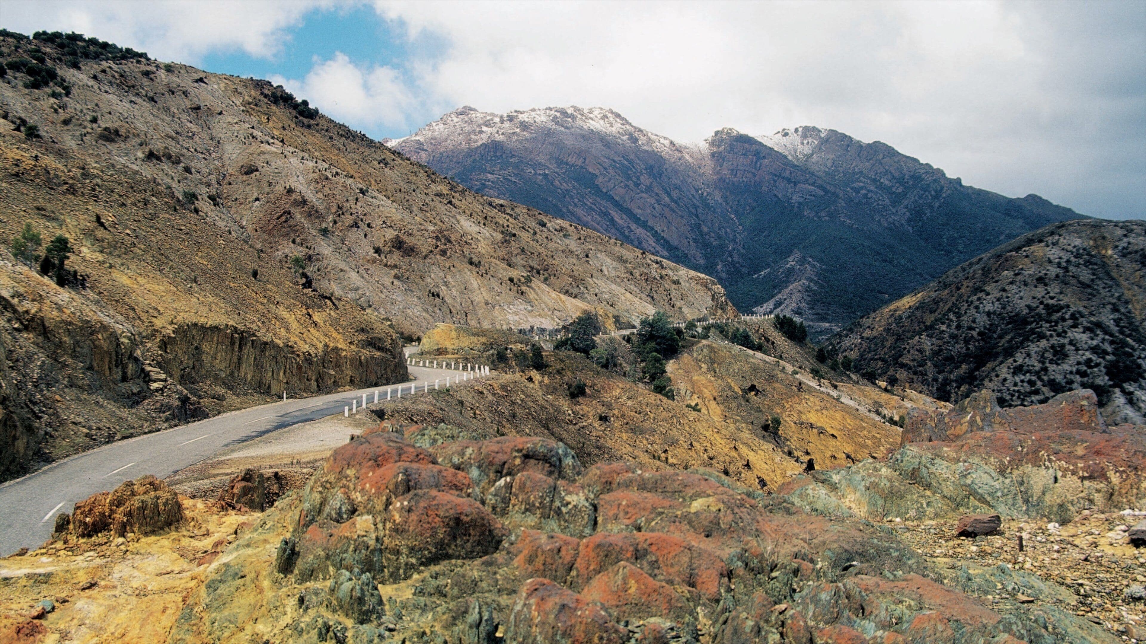 A winding mountain road with rocky terrain and sparse vegetation.