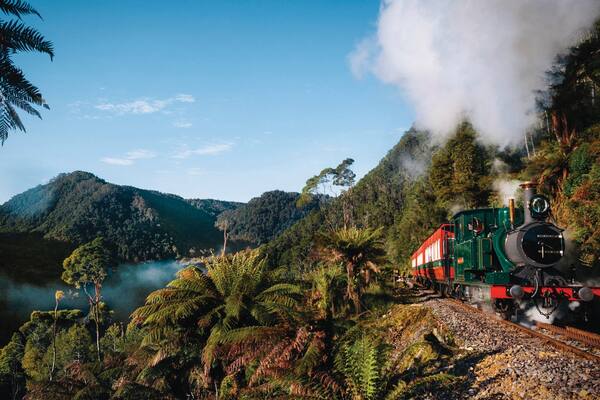 A steam locomotive on a railway track surrounded by lush greenery and mountains.