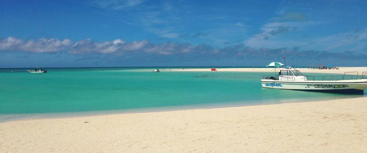 A beach with clear turquoise water, a boat, and a sandy shore.