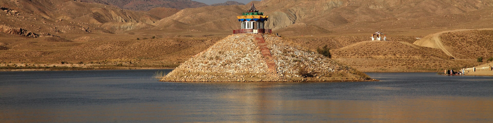 A small island with a traditional building in the center, surrounded by a desert landscape and a clear sky.