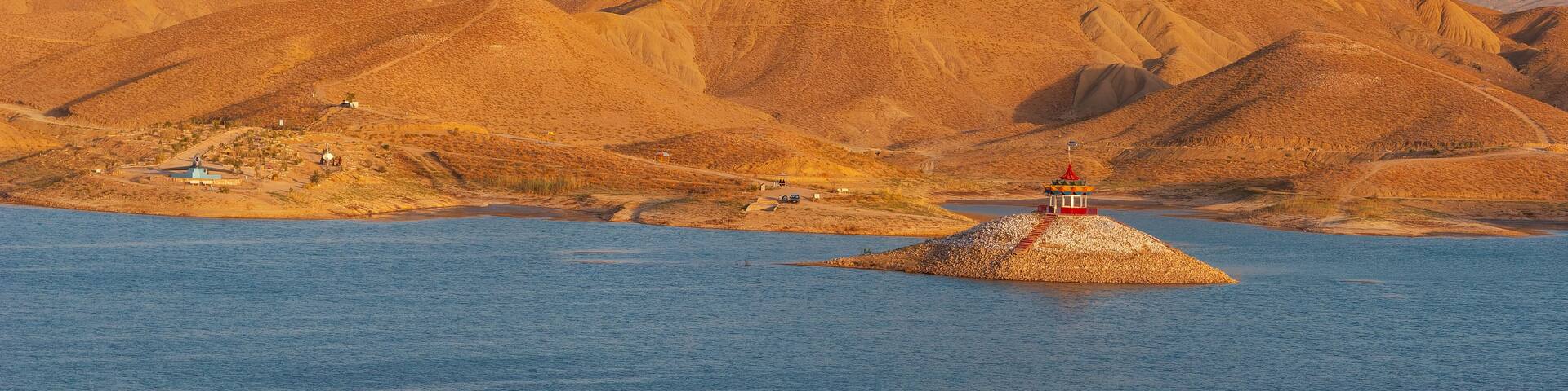 A small island with a lighthouse in the middle of a calm body of water, surrounded by a mountainous landscape.