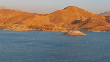Una pequeña isla con un faro en el centro de una masa de agua tranquila, rodeada por un paisaje montañoso.
