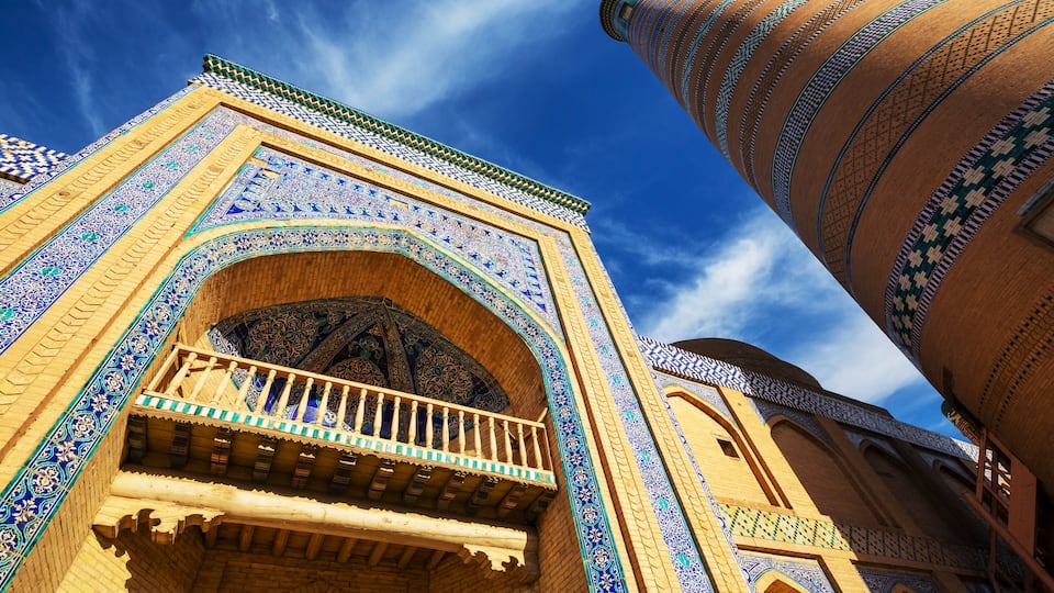 A historic building with intricate blue and green tile work, a balcony, and a tall, slender minaret.