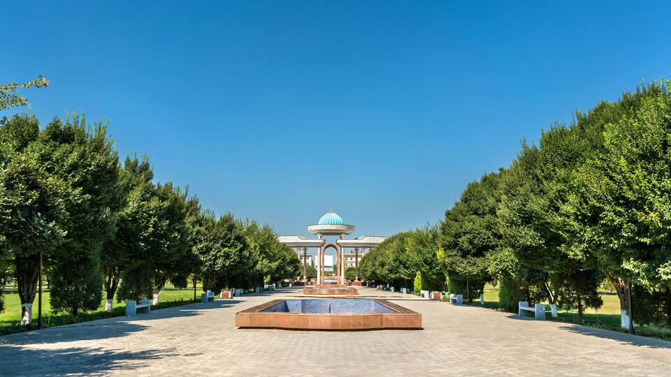 A fountain with a blue-tiled basin, flanked by trees and a building with a dome in the background.