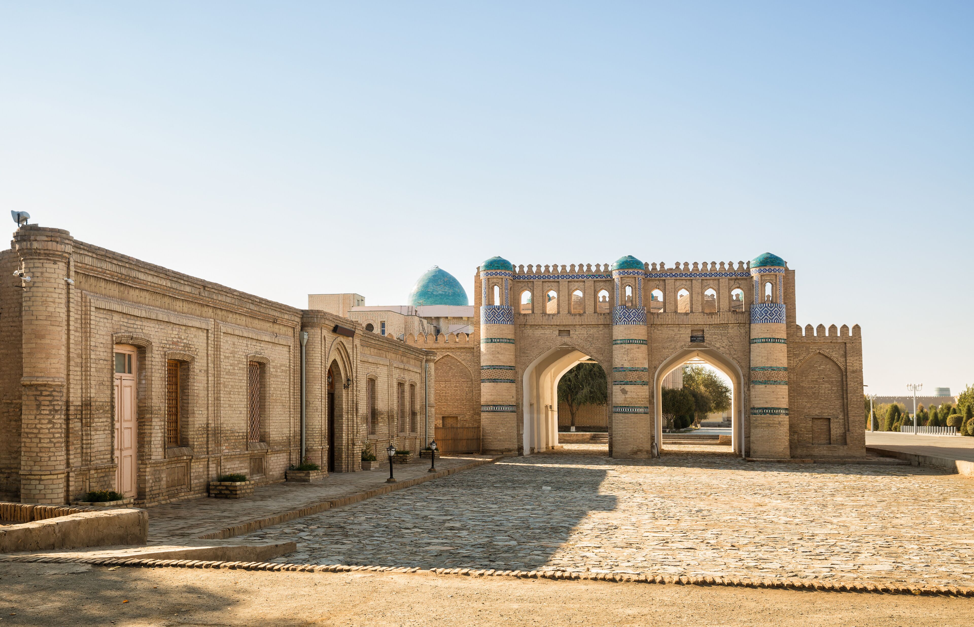 A historic stone archway with intricate patterns, leading to a courtyard with a dome in the background.