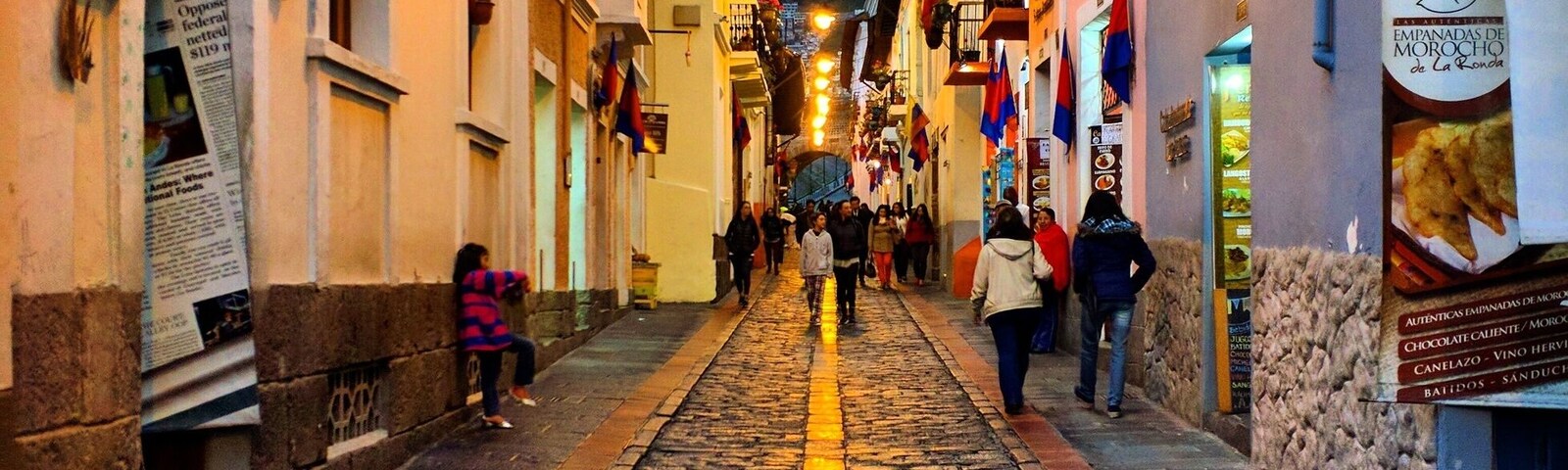 Una calle adoquinada bordeada de edificios, banderas y plantas colgantes.
