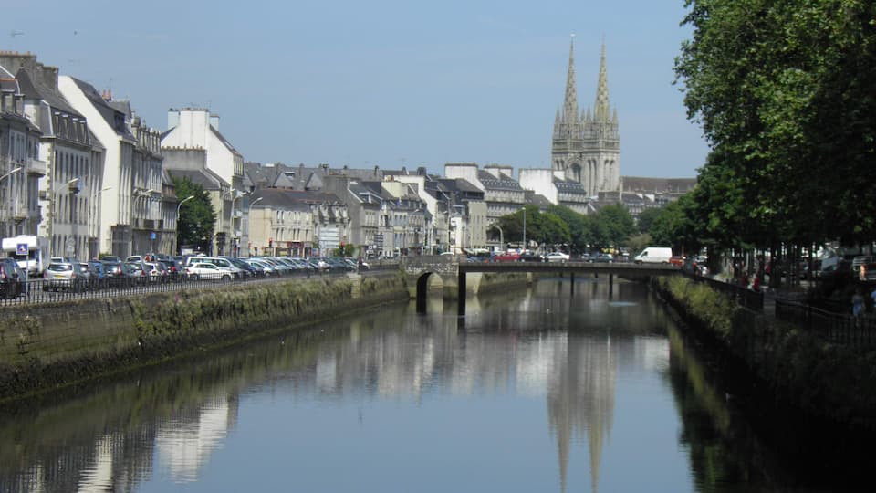 A river reflecting buildings and a cathedral in the distance.