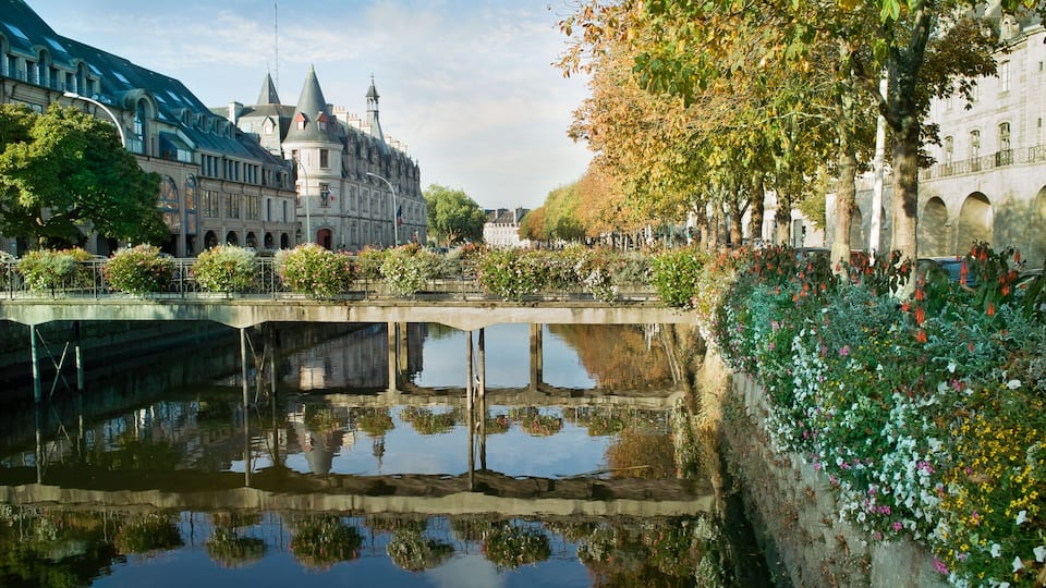 A historic building with a tower, a bridge over a canal, and a flower-lined walkway.