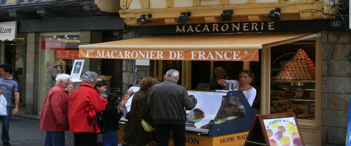 A street food vendor named '1er MACARONIER DE FRANCE' with a signboard and a display of macarons.