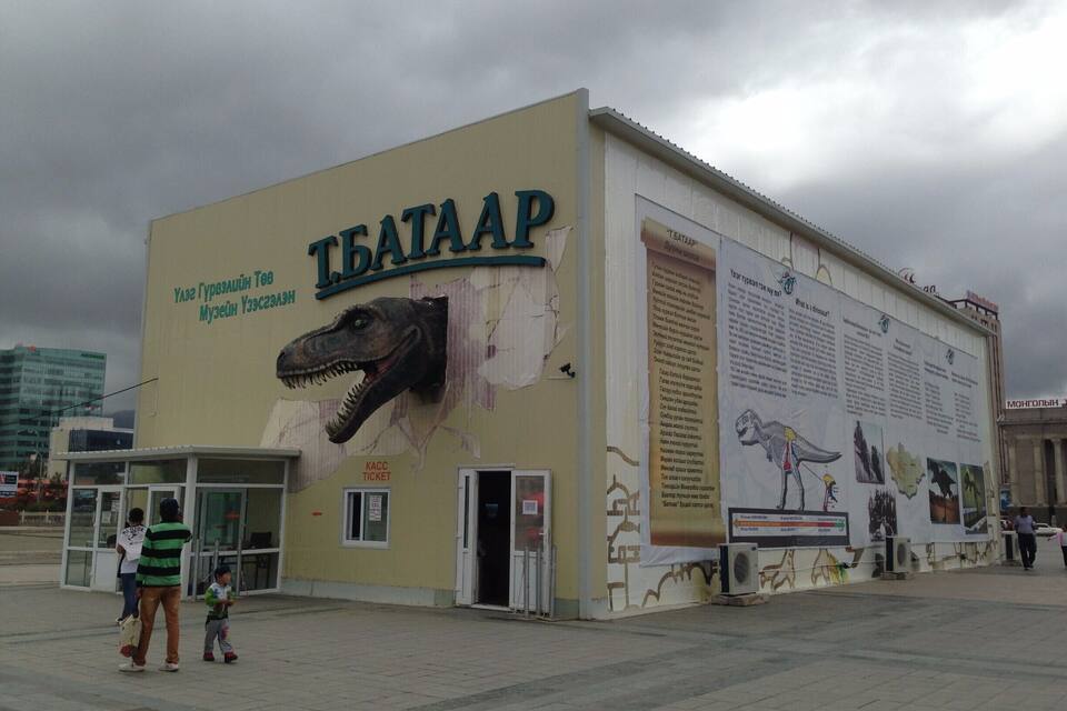 Un edificio de museo con un gran mural de dinosaurios y carteles informativos.