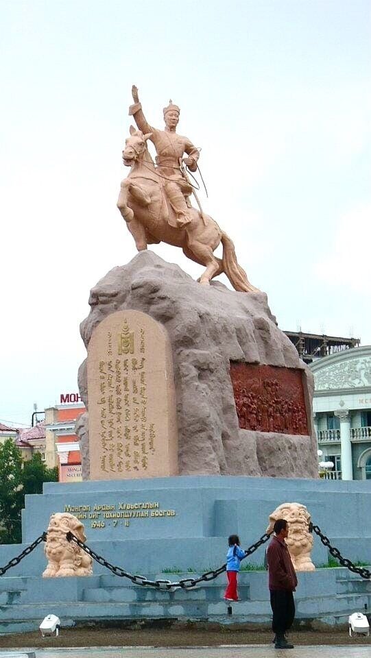 A statue of a mounted figure on a rock pedestal with inscriptions, surrounded by chains and a smaller lion statue.