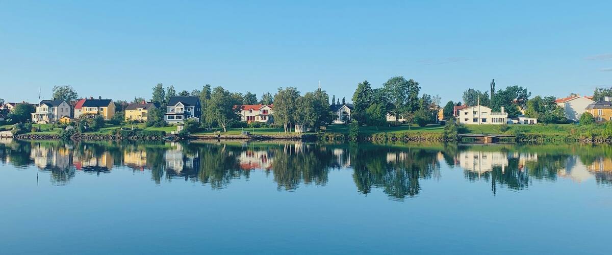 A calm lake reflecting houses and trees under a clear sky.