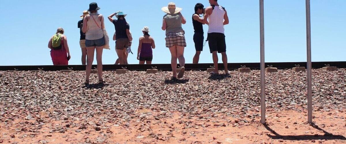 A group of people standing on a rocky terrain with a warning sign about unexploded ordnance.