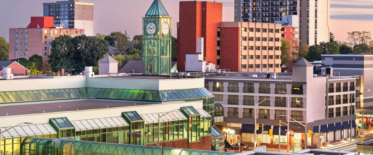 A cityscape with a distinctive green clock tower, modern buildings, and a glass-roofed structure.