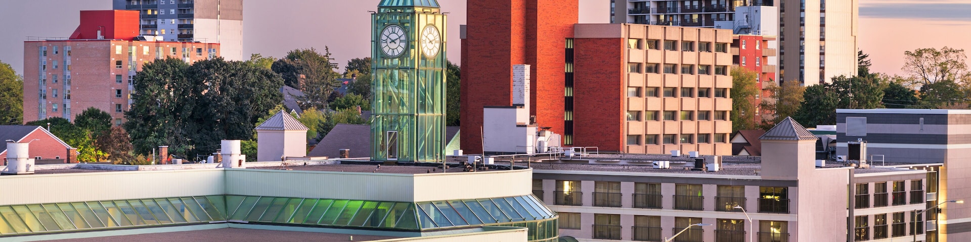 A cityscape with a distinctive green clock tower, modern buildings, and a glass-roofed structure.