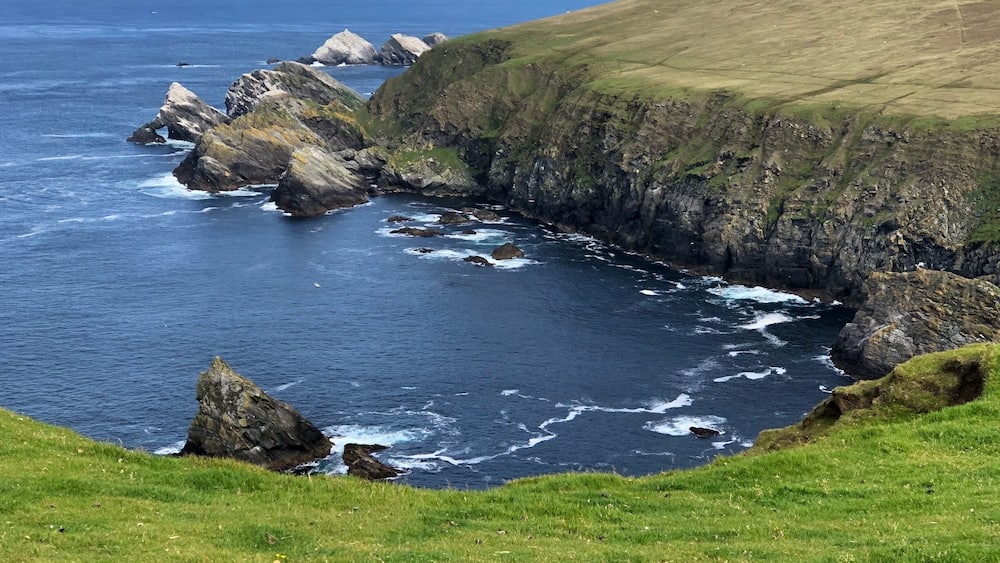 Eine Küstenlandschaft mit felsigen Klippen und grünen Hügeln.
