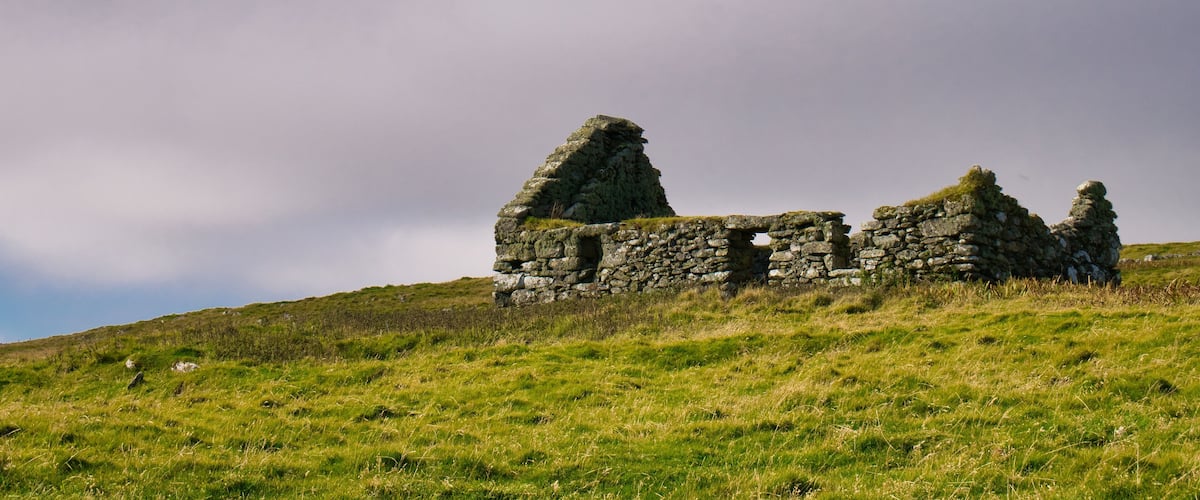 A stone ruin on a grassy hill under a cloudy sky.