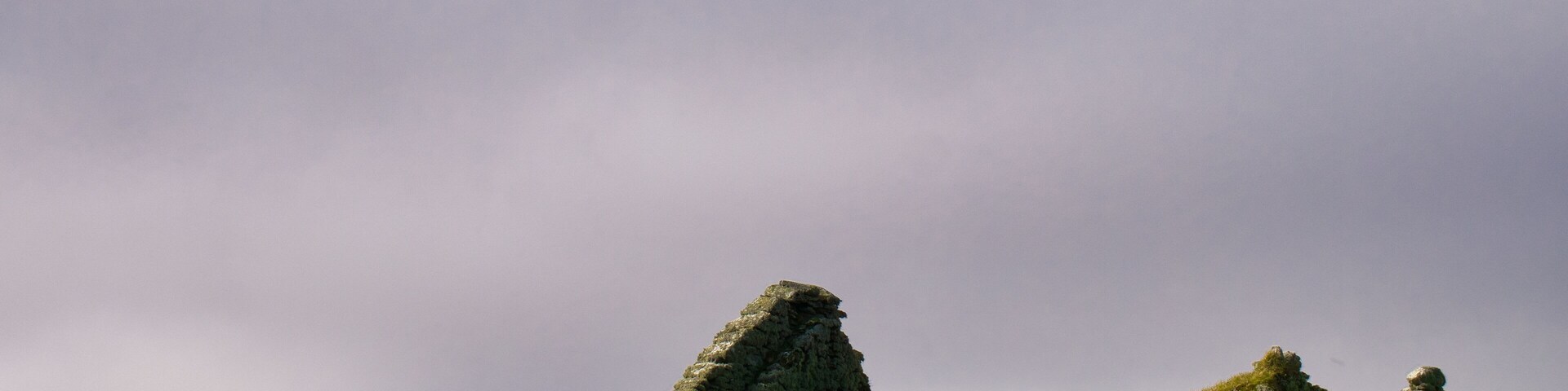 A stone ruin on a grassy hill under a cloudy sky.
