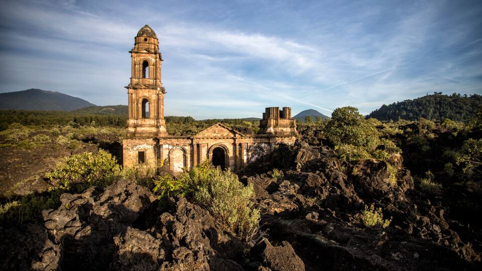 An ancient stone church with a bell tower amidst a rugged volcanic landscape.