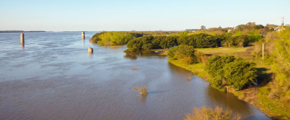 A river with calm water, surrounded by greenery and a few structures.