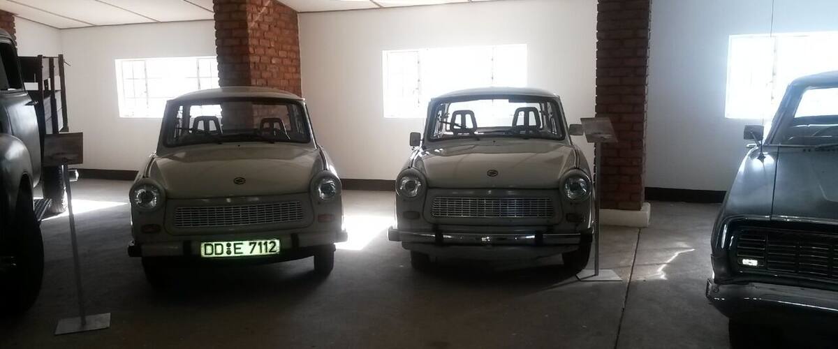 Three vintage cars parked indoors with brick pillars and large windows.