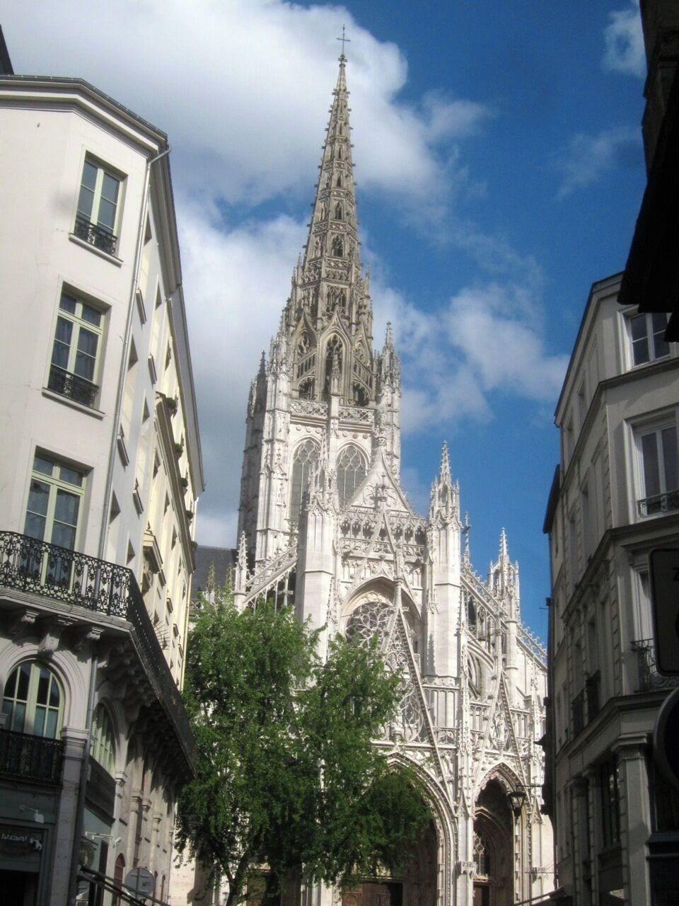 Eine gotische Kathedrale mit aufwendiger Architektur, umgeben von modernen Gebäuden und Bäumen.
