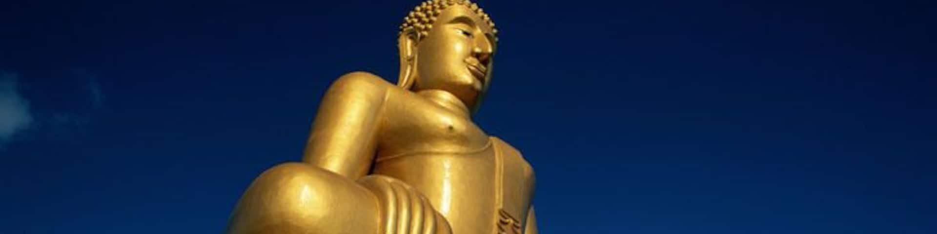 Uma grande estátua dourada de Buda com base vermelha e branca, ao fundo um céu azul límpido.