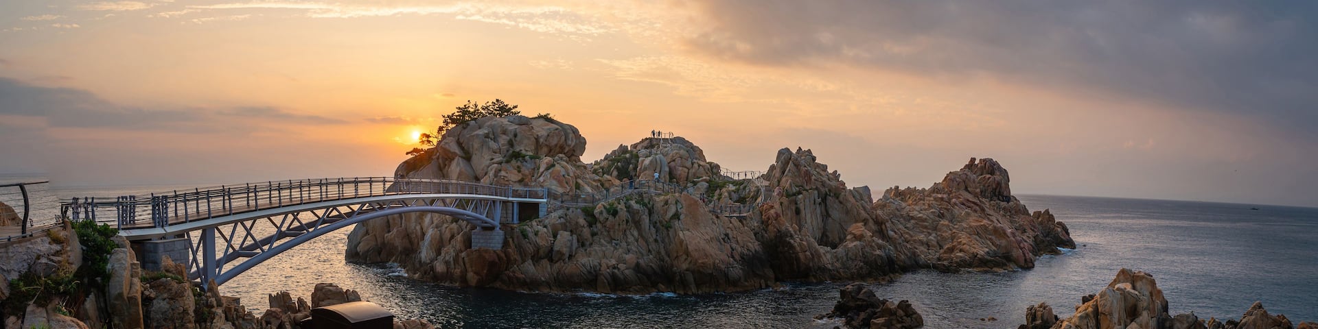 A coastal landscape with a bridge, rocky formations, and the ocean.