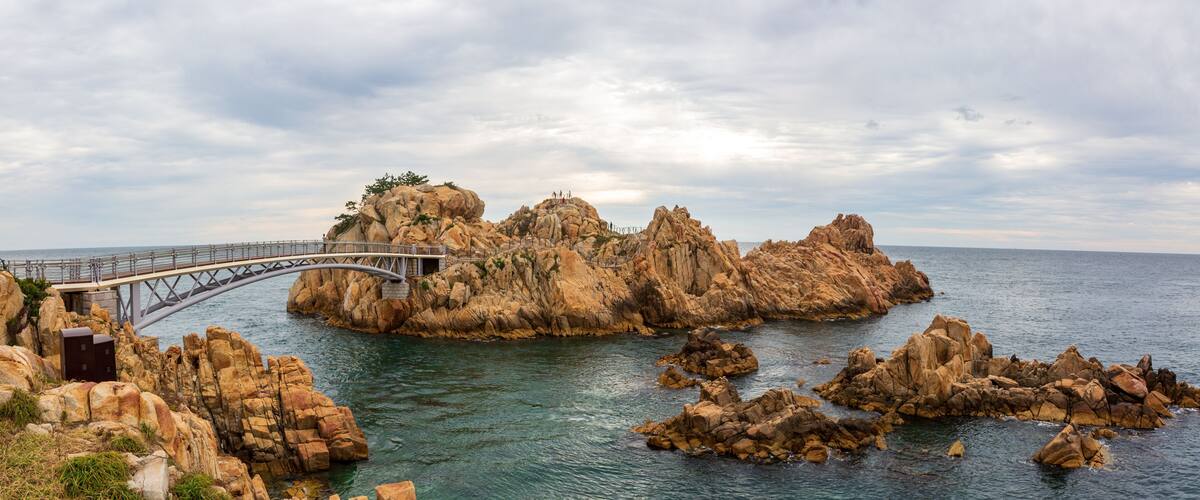 A coastal landscape with a bridge, rocky formations, and a clear sky.