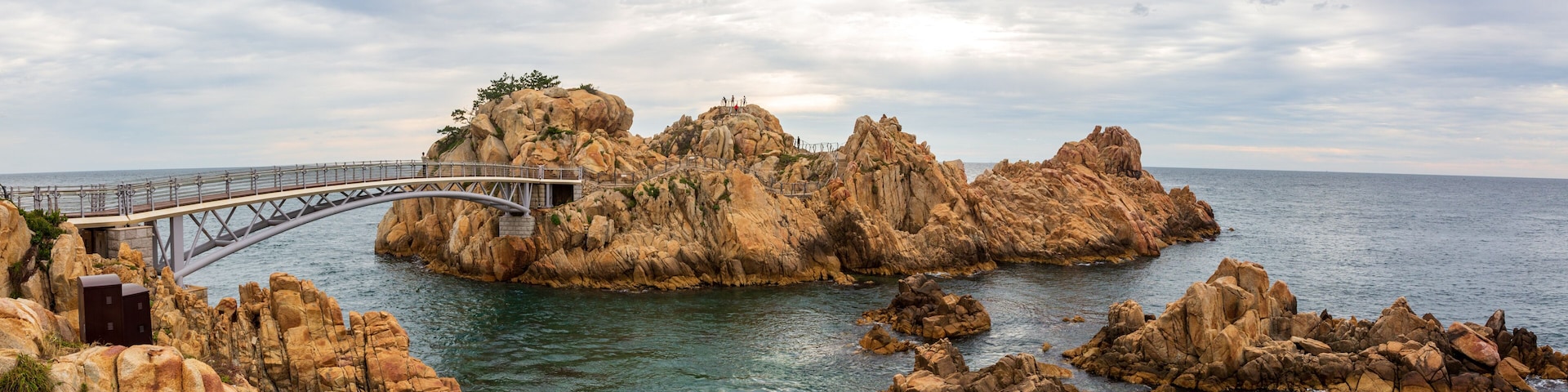 A coastal landscape with a bridge, rocky formations, and a clear sky.