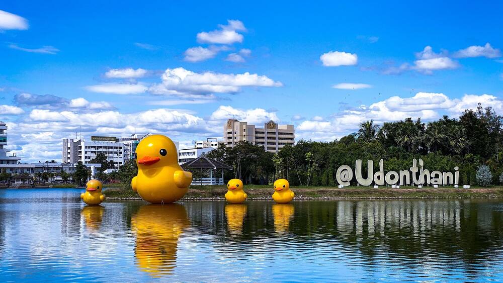 A large yellow duck sculpture in a body of water with a cityscape in the background.