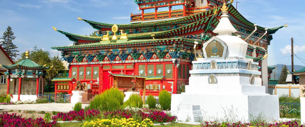 A traditional multi-tiered pagoda with ornate decorations and a white stupa in front.