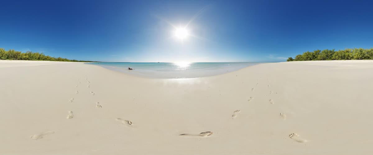 A wide sandy beach with footprints leading towards the ocean under a clear blue sky.