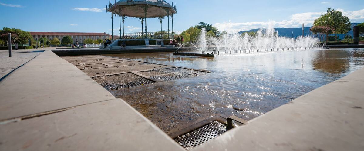 A fountain with water jets, a gazebo, and a clear blue sky.