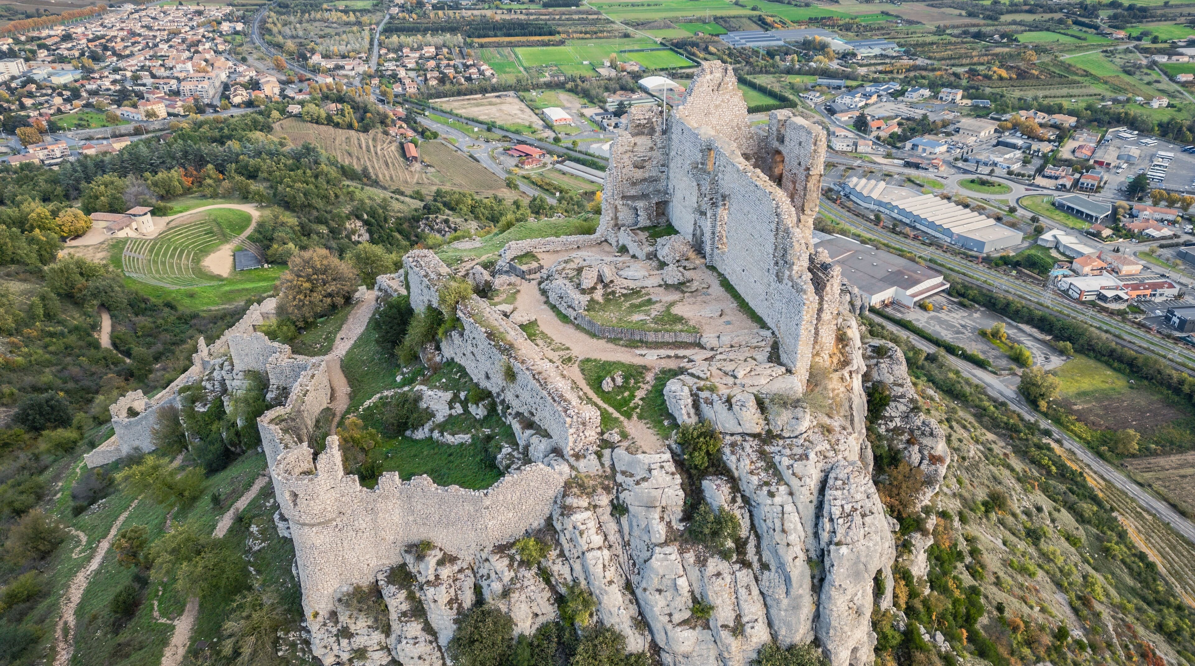 An aerial view of a historic castle ruin surrounded by lush greenery and a modern town.