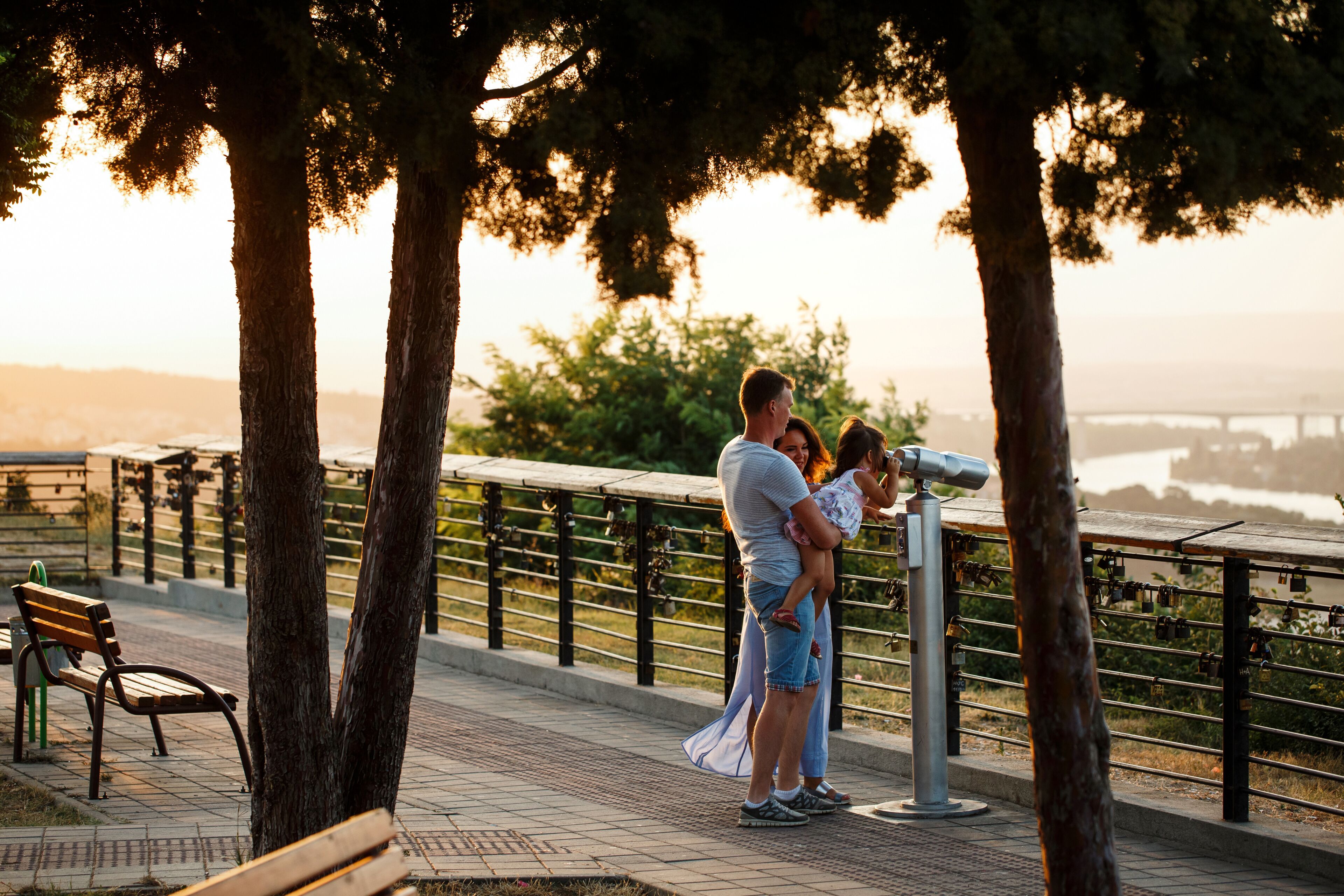 Traditional full family of father, mother and child. Happy couple of parents with a child looking at the sunset on the sea or ocean horizon through binoculars on the observation deck. Bulgaria, Varna