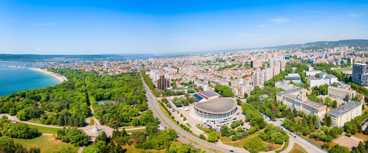 A coastal cityscape with a beach, dense urban area, and a large circular building.